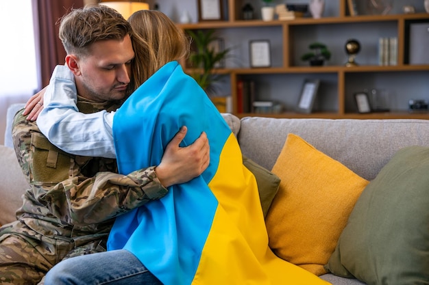 Foto paar sitzt auf dem sofa und umarmt soldat in uniform ist zu hause mit seiner frau flagge der ukraine