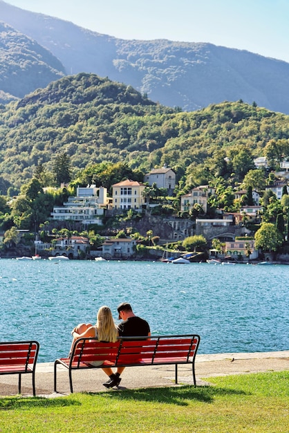 Paar sitzt auf der Bank an der Promenade des teuren Ferienortes in Ascona am Lago Maggiore, Kanton Tessin, Schweiz.