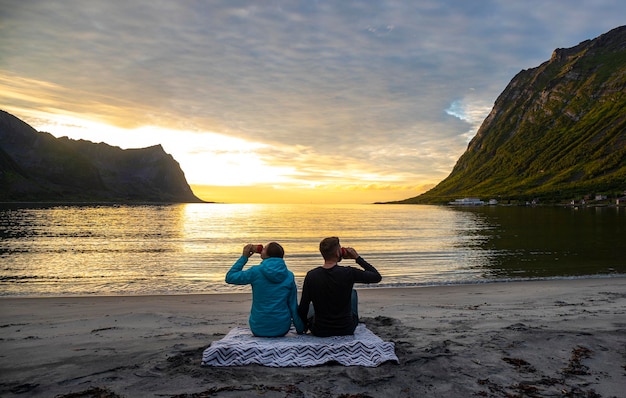 Paar sitzt auf einer Decke am Strand und genießt einen romantischen Sonnenuntergang im norwegischen Fjord Senja