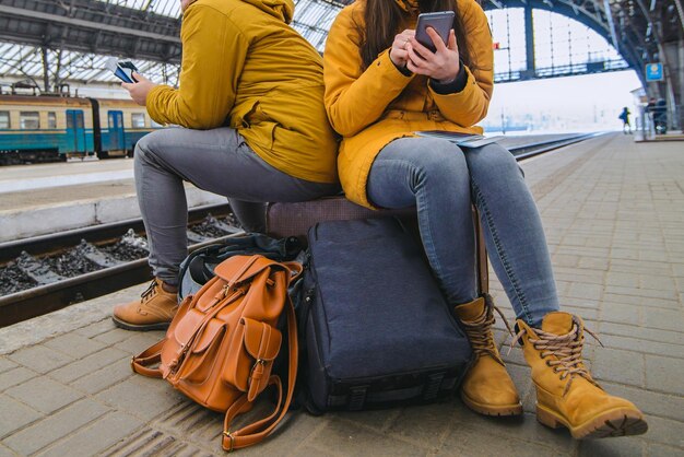 Paar sitzt auf Koffer am Bahnhof. Surfen im Internet, während Sie auf den Zug warten. Reisekonzept