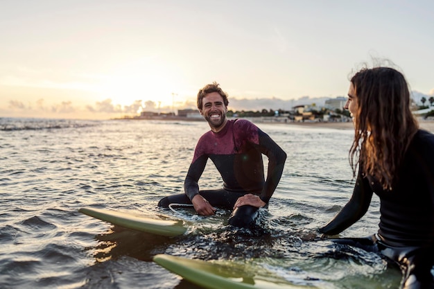 Paar sitzt auf Surfbrettern im Wasser und lächelt in die Kamera