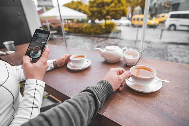 Paar sitzt im Café und trinkt Aufwärmtee an kalten Herbsttagen Frau fotografiert am Telefon für Instagram