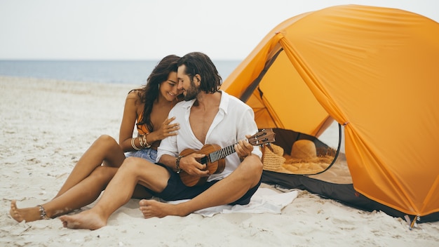 Paar spielt Ukelele mit einem orangefarbenen Zelt am Strand