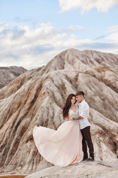 Paar steht auf dem Abgrund des Berges und des roten Sees und umarmt. Die Braut und der Bräutigam in der Liebe, die Frau im langen Kleid in den Armen der Männer