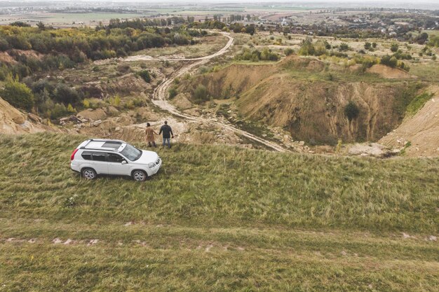 Paar steht bei bewölktem Wetter auf einer Klippe in der Nähe eines weißen Geländewagens