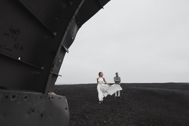 Paar steht in der Nähe des Flugzeugs, das vor langer Zeit am schwarzen Strand abgestürzt ist