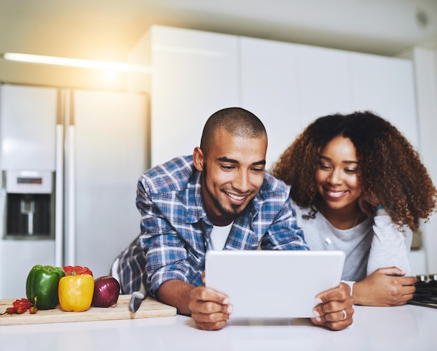 Paar Tablet und Kochen von Essen in der Küche zu Hause mit Blog-Internet-Website und Online-Verbindung. Glücklicher afrikanischer Mann, Frau und digitales Rezept zum Lesen von Anleitungen für gesunde vegetarische Mahlzeiten