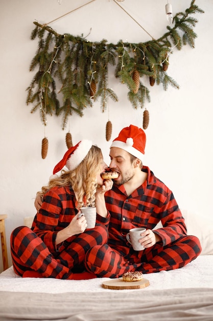 Paar trägt weihnachtlich karierte rote Pyjamas, die auf dem Bett sitzen