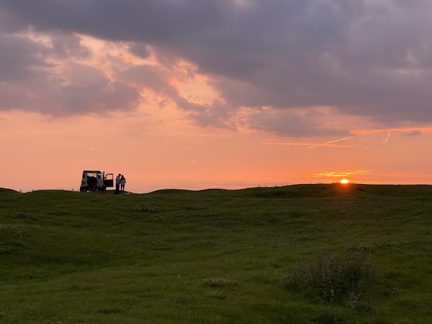 Paar umarmt sich in der Nähe ihres Autos auf dem Hügel und beobachtet den Sonnenuntergang in den Bergen