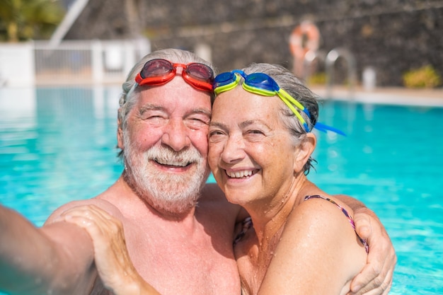 Paar von zwei glücklichen Senioren, die Spaß haben und zusammen im Schwimmbad genießen und ein Selfie-Foto machen, das lächelt und in die Kamera schaut. Glückliche Leute, die den Sommer im Freien im Wasser genießen