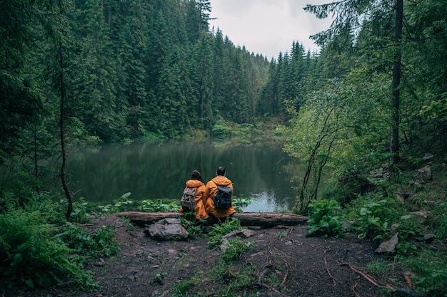 Paar Wanderer im gelben Regenmantel mit Blick auf den Bergsee