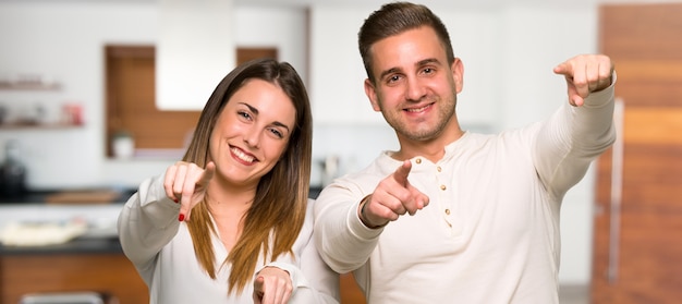 Paar zeigt Finger auf Sie mit einem überzeugten Ausdruck in einem Haus