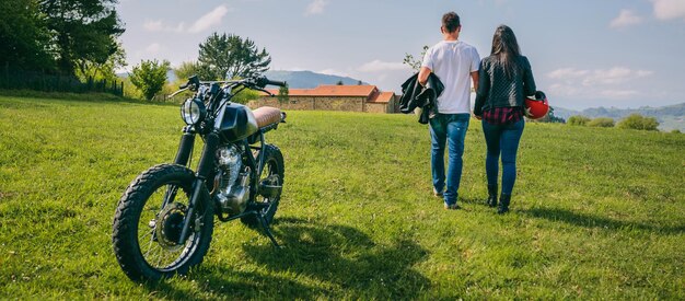 Paar zu Fuß auf dem Feld Händchen haltend und Motorrad