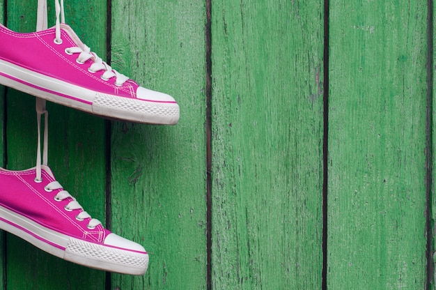 Paare der hellen rosa Sportturnschuhe, die an einer hölzernen Wand hängen, knackten