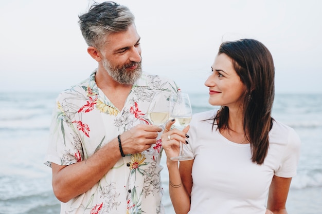 Paare, die ein Glas Wein durch den Strand genießen