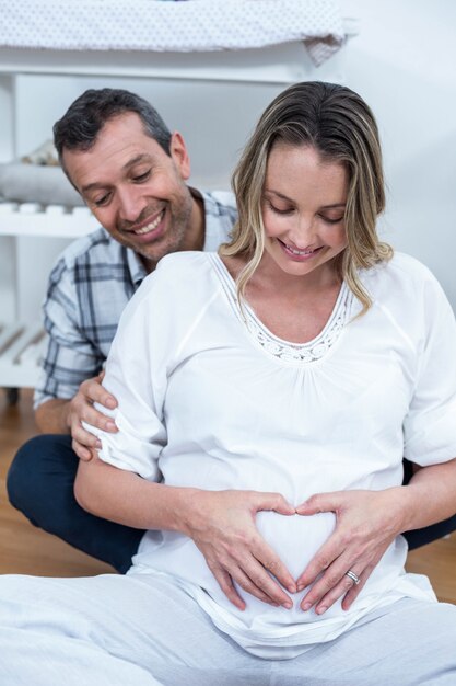 Paare, die ein Herz bilden, formen auf den schwangeren Bauch mit ihren Händen