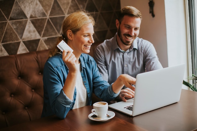 Paare, die online mit Kreditkarte und Laptop in einer Kaffeestube kaufen