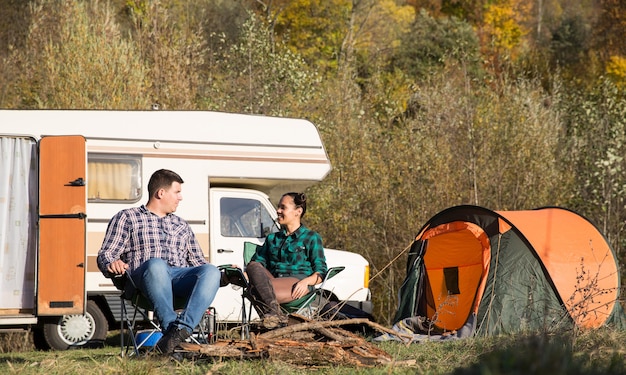 Paare, die sich nach einer langen Reise auf einem Campingplatz mit ihrem Retro-Wohnmobil im Hintergrund entspannen.