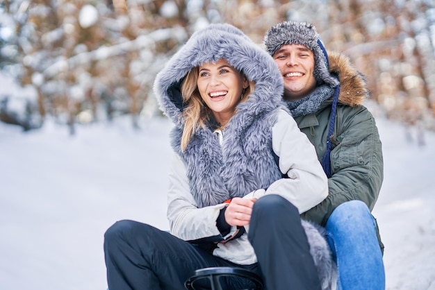 Paare, die Spaß mit Schlitten auf Schnee im Winterschnee haben. Foto in hoher Qualität
