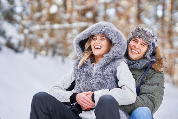 Paare, die Spaß mit Schlitten auf Schnee im Winterschnee haben. Foto in hoher Qualität