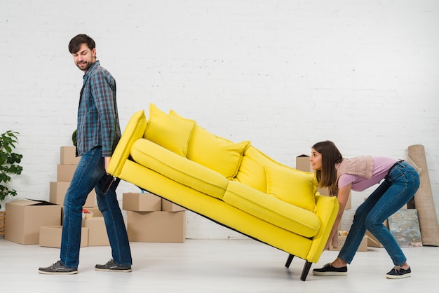 Foto paare, die versuchen, das gelbe sofa in ihr neues haus zu setzen