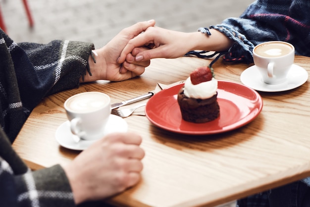 Paare im Café-Händchenhalten-Erdbeerkleinen kuchen.