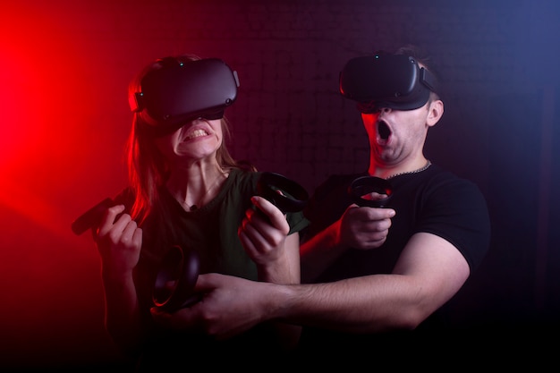 Paare in den modernen Gläsern der virtuellen Realität spielen einen Schützen gegen einen dunklen Neonhintergrund, ein Team der Spieler in einem Spiel mit Waffen