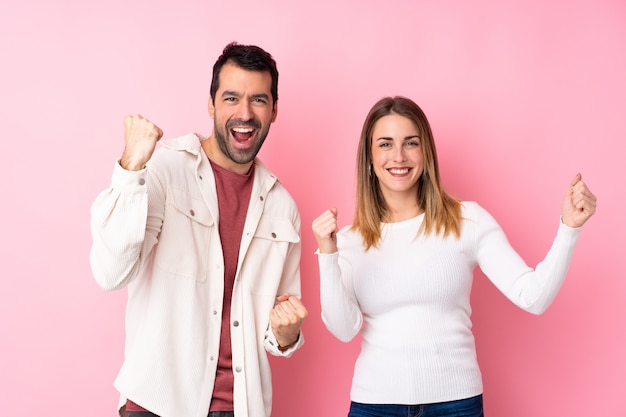 Paare in Valentine Day über der lokalisierten rosa Wand, die einen Sieg feiert