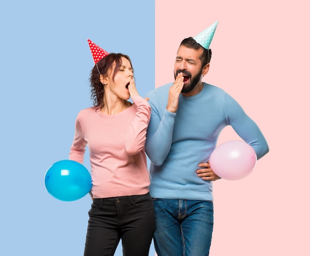 Paare mit den Ballonen und Geburtstagshüten, die Mund mit der Hand gähnen und bedecken.