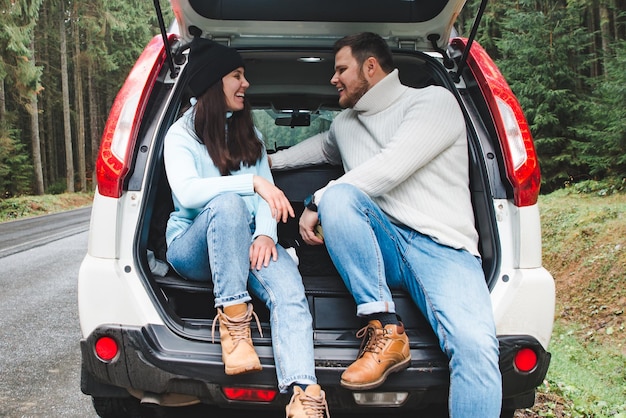 Paare stoppen, um heißen Tee zu trinken. Roadtrip-Konzept. im suv-kofferraum am straßenrand im bergwald sitzen. Lebensstile