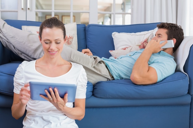Paare unter Verwendung der digitalen Tablette und des Mobiltelefons im Wohnzimmer
