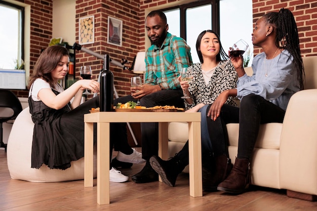 Paare verschiedener ethnien trinken wein, alkohol und sitzen im wohnzimmer der wohnung.