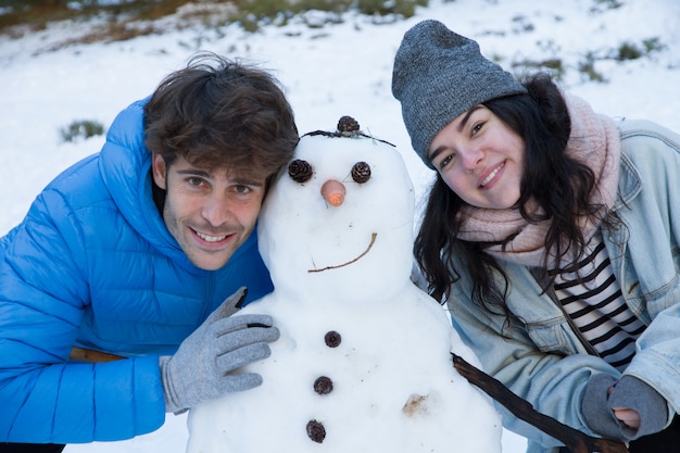 Paare von den Liebhabern, die im Schnee mit einem Schneemann genießen.