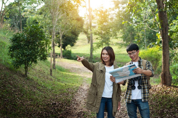 Paare von den Touristen, die in der Hand zum Wald mit Karten vorangehen