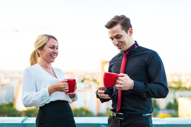 Paare von Geschäftsmännern, von attraktivem Brunettemann und von hübschen Blondinen stehen auf dem Dach und trinken Kaffee