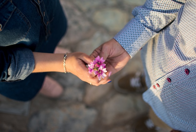 Paarhände mit Blumen bei Sonnenuntergang