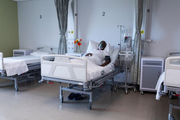 Paciente afro-americano deitado na cama do hospital usando ventilador com máscara de oxigênio