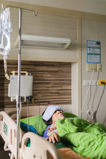 Foto paciente anciana acostada en la cama en el hospital con compresa en la frente