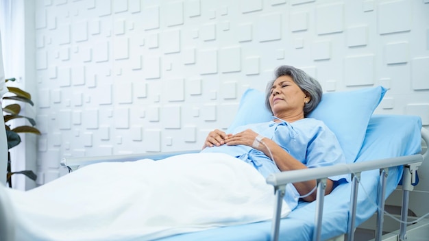 Foto paciente anciana acostada en la cama recibiendo solución salina en la habitación del paciente cansada de los síntomas de la enfermedad