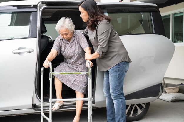 Una paciente anciana asiática camina con un andador y se prepara para llegar a su auto, un concepto médico fuerte y saludable