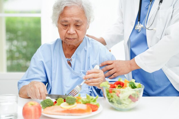 Paciente anciana asiática comiendo salmón y ensalada de verduras para una comida saludable en el hospital