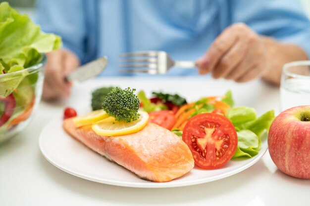 Paciente anciana asiática desayunando bistec de salmón con comida saludable vegetal en el hospital