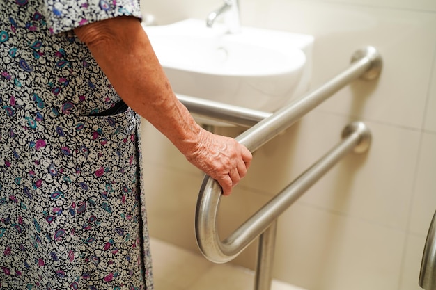 Paciente anciana asiática usa el riel de soporte del inodoro en la barandilla de seguridad del baño
