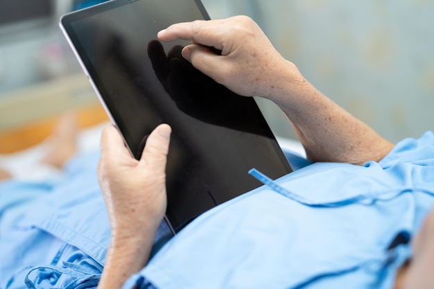 Foto paciente asiática idosa ou idosa segurando em suas mãos um tablet digital e lendo e-mails enquanto está sentada na cama na ala do hospital de enfermagem saudável conceito médico forte