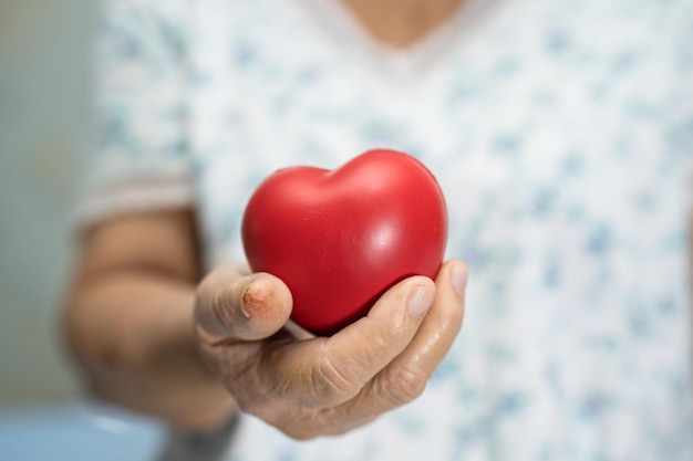 Paciente asiática mayor o anciana anciana con corazón rojo en la mano en la cama en la sala del hospital de enfermería concepto médico fuerte y saludable