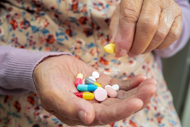 Paciente asiática mayor que sostiene pastillas de cápsulas de antibióticos para pacientes con infección de tratamiento en el hospital, concepto de farmacia.