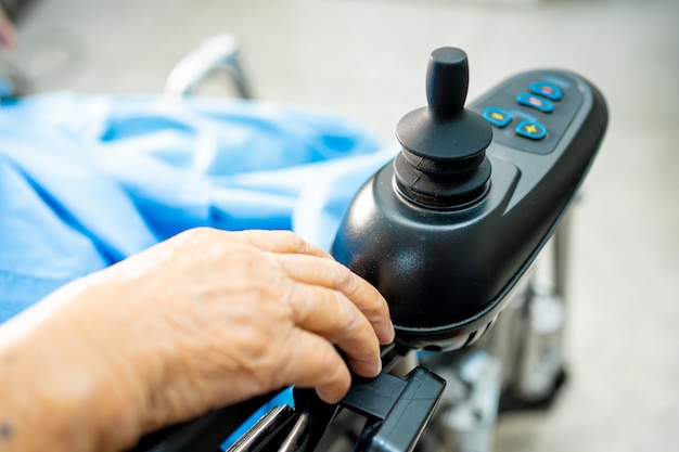 Paciente asiático mayor de la mujer en la silla de ruedas eléctrica con control remoto en el hospital.