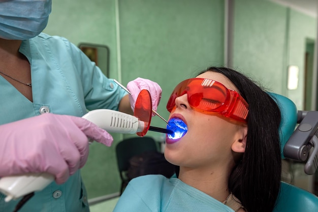 Paciente con la boca abierta sentado en la silla del dentista con gafas protectoras