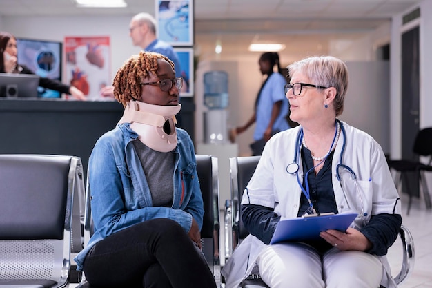 Paciente com colar cervical médico na consulta com o médico, sentado no saguão da sala de espera. Mulher com espuma cervical e médico sênior preenchendo papéis de relatório de check-up na consulta no hospital.