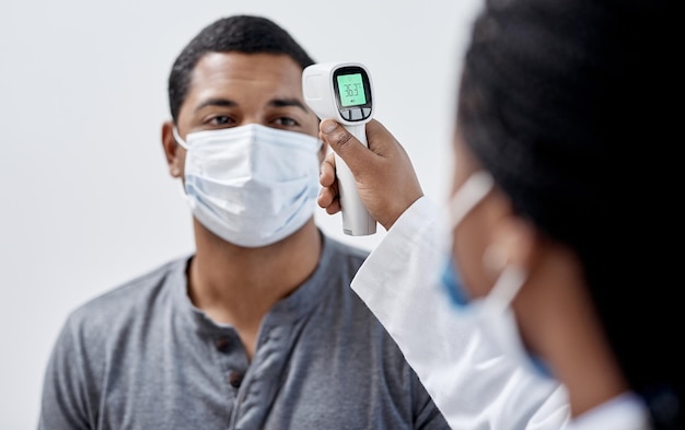 Paciente covid masculino a quien un médico le toma la temperatura con equipo médico en la sala de consulta del hospital Hombre con máscara y profesional de la salud que señala el termómetro infrarrojo digital